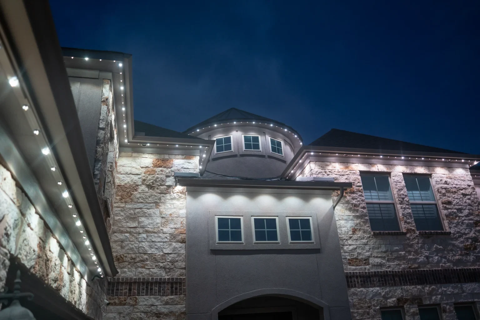 Close-up of small permanent lights spaced along a stone home's eaves at night